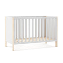 Cuna infantil blanca con laterales de barrotes y estructura de madera clara; diseño sencillo de tablas continuas.