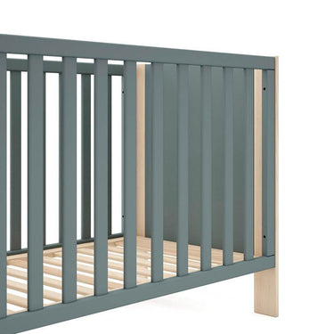 Cuna infantil de madera con acabado verde kaki y detalles en tono natural, barrotes verticales y somier de láminas de pino.