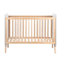 Cuna infantil de madera clara con barrotes verticales y somier de láminas; extremos superiores blancos y diseño sencillo.