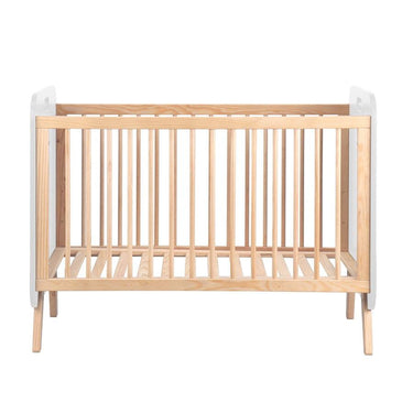 Cuna infantil de madera clara con barrotes verticales y somier de láminas; extremos superiores blancos y diseño sencillo.