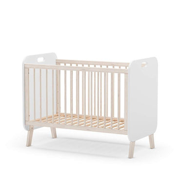Cuna infantil blanca con barrotes verticales, laterales sólidos con asas y patas inclinadas de madera clara.