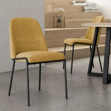 Silla de comedor en tono mostaza, tapizada con textura y respaldo curvo, patas metálicas negras de líneas rectas.