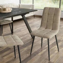 Silla de comedor tapizada en tejido beige con acolchado de cuadrantes y patas metálicas negras finas.