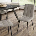 Silla de comedor gris con tapizado de tejido capitoné en cuadrantes y patas metálicas negras inclinadas.