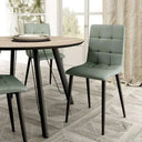 Silla de comedor verde salvia tapizada en tejido liso, con respaldo acolchado en cuadrantes y patas metálicas negras.