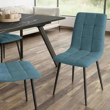 Silla de comedor azul turquesa con tapizado de tejido capitoné en cuadrantes y patas metálicas negras delgadas.