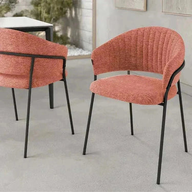 Silla de comedor tapizada en tela salmón con respaldo curvado y patas metálicas negras de diseño moderno y líneas finas.