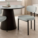 Silla de comedor tapizada en gris claro, con asiento y respaldo acolchados y patas rectas de metal negro.