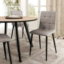 Silla de comedor gris claro tapizada en cuadrantes capitoné, con respaldo alto y patas metálicas negras.