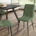 Silla de comedor verde de tela, con respaldo y asiento acolchados en cuadrantes y patas metálicas negras.