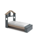 Cama infantil gris con detalles de madera natural, cabecero en forma de casa con estante y arcón al pie.