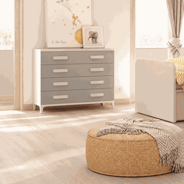 Cómoda dormitorio de cuatro cajones en tonos gris y blanco, con tiradores ovalados claros y patas cortas.