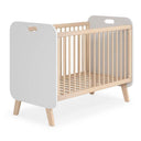 Cuna infantil de paneles blancos y estructura de madera clara, con barrotes verticales, patas inclinadas y somier de láminas.