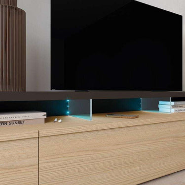 Mueble salón de televisión en acabado madera clara, con frentes texturizados, tiradores integrados y soporte elevado con LED azules.
