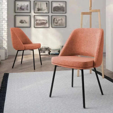 Silla de comedor tapizada en salmón, con asiento acolchado, respaldo envolvente y patas metálicas negras.