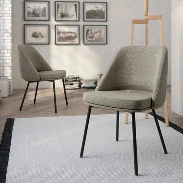 Silla de comedor tapizada en gris texturizado, con asiento acolchado, respaldo envolvente y patas metálicas negras.