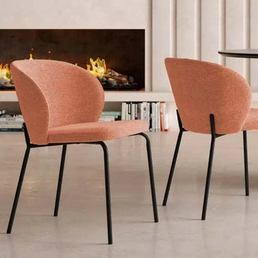 Silla de comedor en tapizado salmón texturizado, con respaldo curvo envolvente y patas negras de hierro.