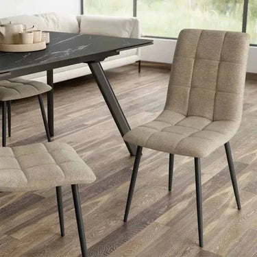 Silla de comedor tapizada en tejido beige con acolchado de cuadrantes y patas metálicas negras finas.