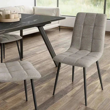 Silla de comedor gris con tapizado de tejido capitoné en cuadrantes y patas metálicas negras inclinadas.