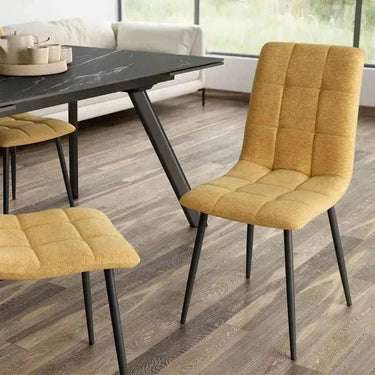 Silla de comedor mostaza con tapizado texturizado en cuadrantes capitoné y patas metálicas negras estilizadas
