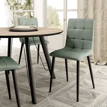 Silla de comedor verde salvia tapizada en tejido liso, con respaldo acolchado en cuadrantes y patas metálicas negras.