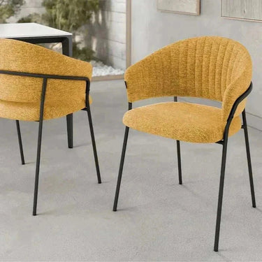 Silla de comedor tapizada color mostaza con respaldo curvado y patas metálicas negras, diseño de líneas finas.