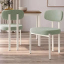 Silla de comedor tapizada en tela verde claro con patas blancas de metal, diseño moderno y respaldo ovalado acolchado.