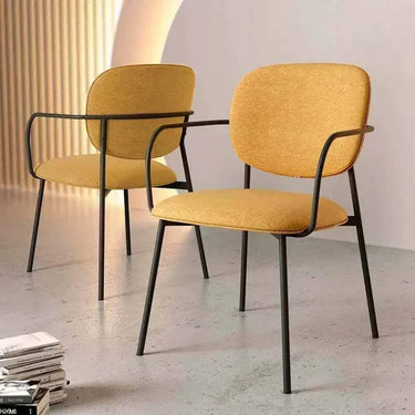 Silla de comedor tapizada mostaza con reposabrazos, asiento acolchado y patas metálicas negras en pack de 2 unidades.
