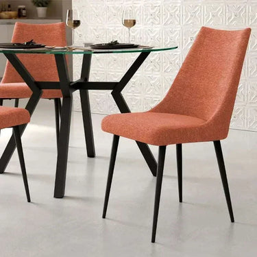Silla de comedor en tono salmón, con asiento y respaldo tapizados y patas metálicas negras de diseño moderno.