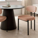 Silla de comedor tapizada en tono salmón rosado, con asiento y respaldo acolchados y patas metálicas negras de líneas rectas.
