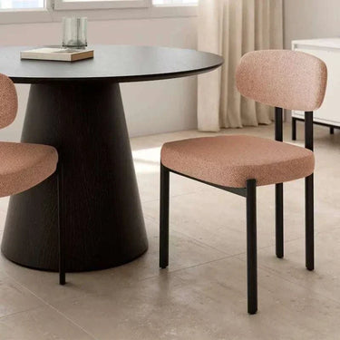Silla de comedor tapizada en tono salmón rosado, con asiento y respaldo acolchados y patas metálicas negras de líneas rectas.