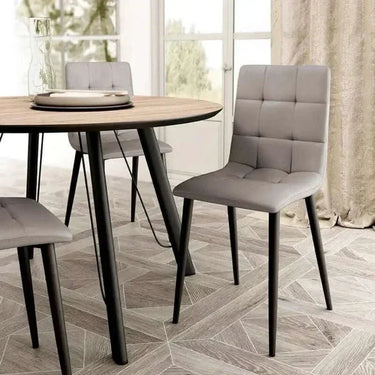 Silla de comedor gris claro tapizada en cuadrantes capitoné, con respaldo alto y patas metálicas negras.