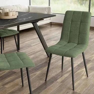 Silla de comedor verde de tela, con respaldo y asiento acolchados en cuadrantes y patas metálicas negras.