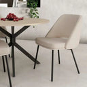 Silla beige tapizada en tejido liso, con asiento acolchado, respaldo curvo y patas metálicas negras.